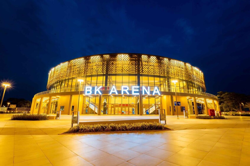 A modern, circular building with 'BK ARENA' illuminated signage, surrounded by a well-lit plaza. 1