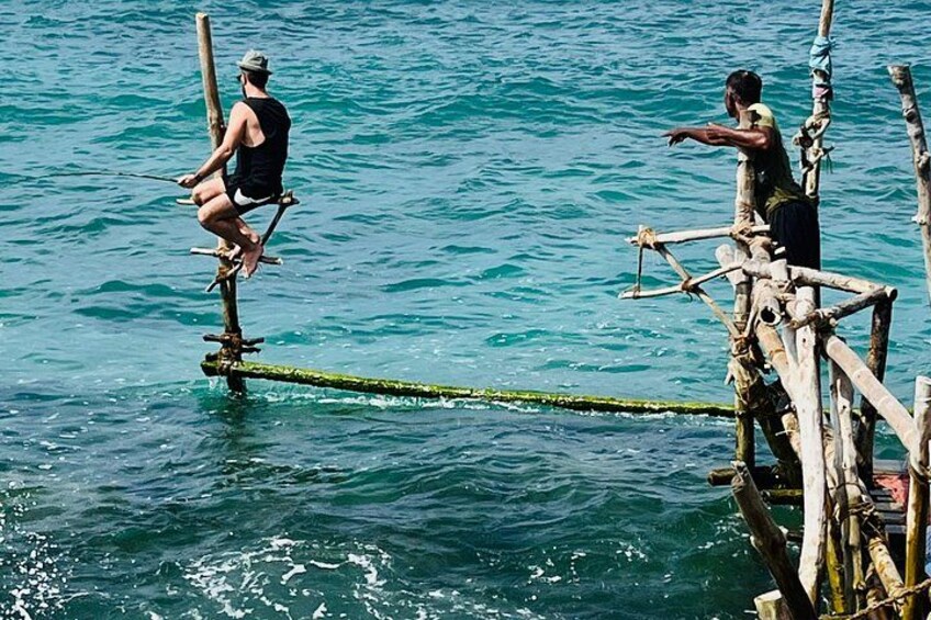 Two individuals balancing on a narrow wooden plank over water, connected by a rope. 2
