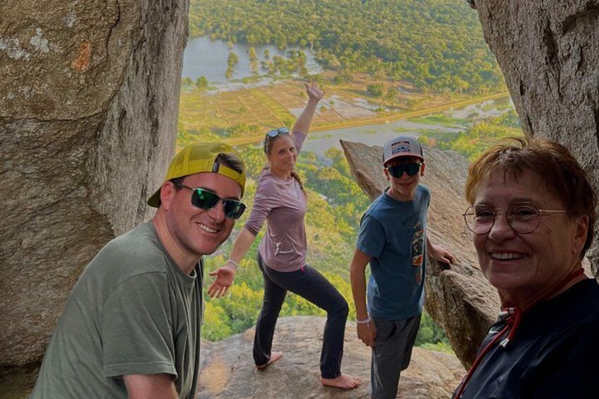 Three people standing on a rocky outcrop with a scenic view of a valley and river. 5