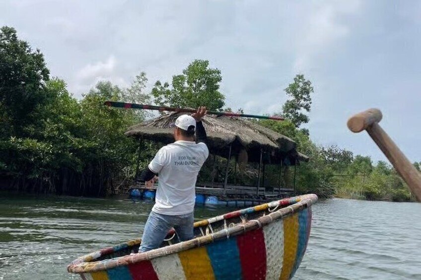 A person paddling a colorful boat with a thatched roof structure on a calm river surrounded by dense greenery. 1