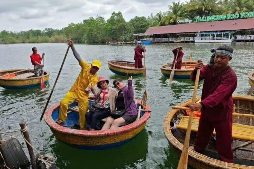 People in traditional boats on a river, with a building in the background. 4