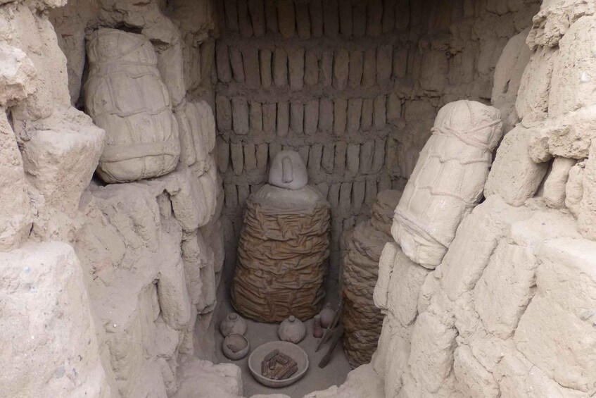 A narrow passageway with a large, cylindrical stone structure in the center, flanked by smaller stones and a bowl at the bottom. 2