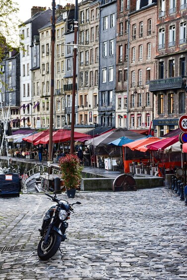 A cobblestone street with a parked motorcycle, buildings, and outdoor cafes. 2