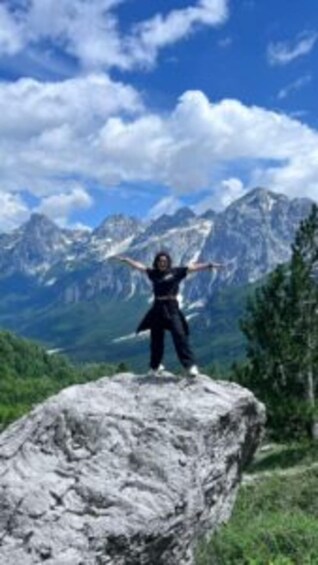 A person standing on a rock with arms outstretched, surrounded by mountains and a clear sky. 3
