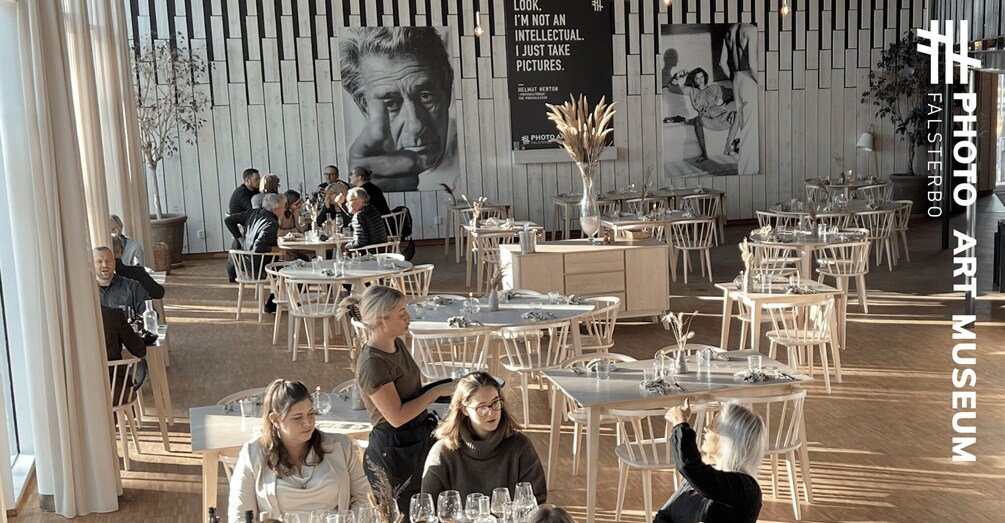 An indoor art museum with white walls, black-and-white photographs, and round tables. 1