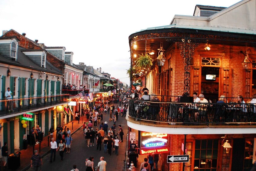 A bustling street with people walking, a balcony restaurant, and various storefronts. 1