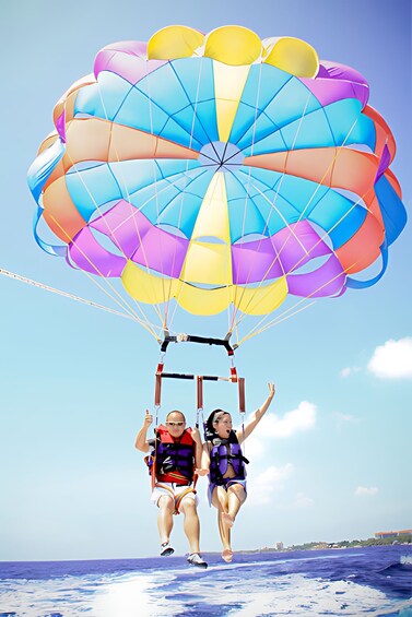 Two people parasailing over the ocean with a colorful parachute. 4