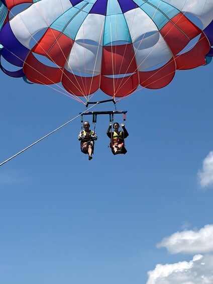 Two people paragliding with a colorful parachute against a clear blue sky. 1