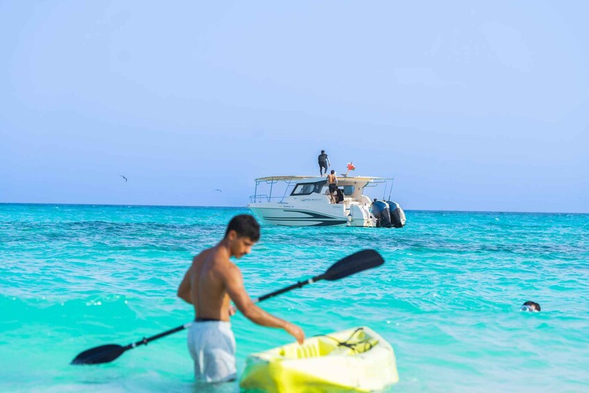 A man in a kayak on turquoise water, a boat with people on it, and a swimmer in the water. 5