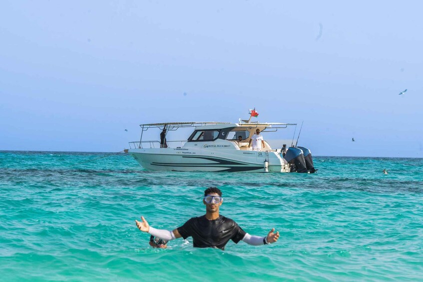 A person swimming in turquoise water with a boat in the background. 4