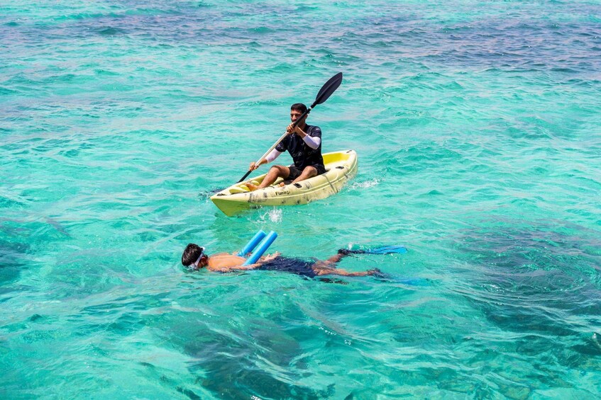 A person kayaking in turquoise water, another person swimming with a blue float, and a third person paddling a yellow kayak. 3