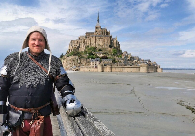 A person in medieval costume standing on a beach with a historic castle in the background. 1