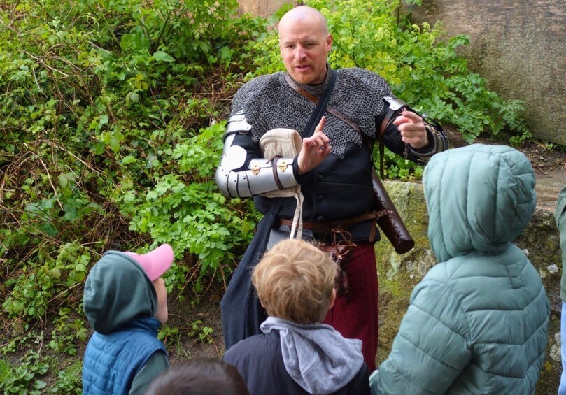 A person in medieval armor gesturing to a group of children. 2