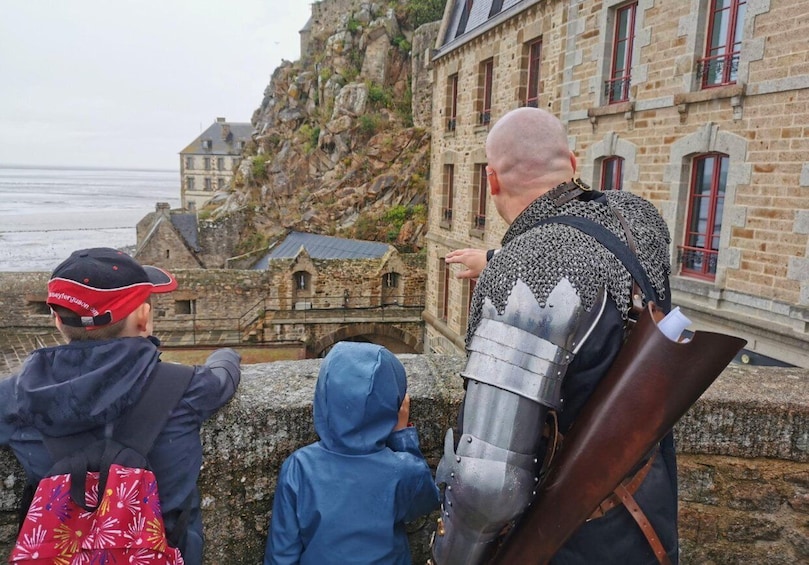 A person in medieval armor overlooking a coastal town with stone buildings and a cliff. 3