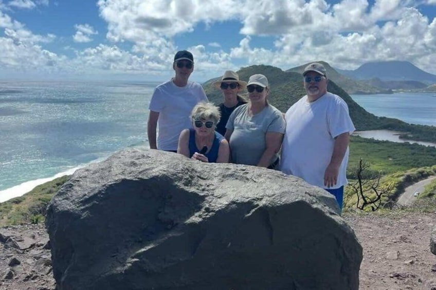 A group of people standing on a rocky outcrop with a view of the ocean and a mountainous landscape in the background. 3