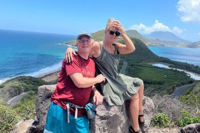 Two people sitting on a rocky outcrop with a coastal landscape in the background. 3