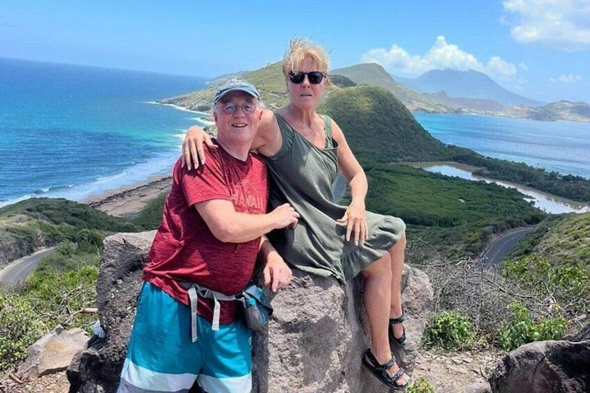 Two people sitting on a rocky outcrop with a view of the ocean and a road in the background. 3