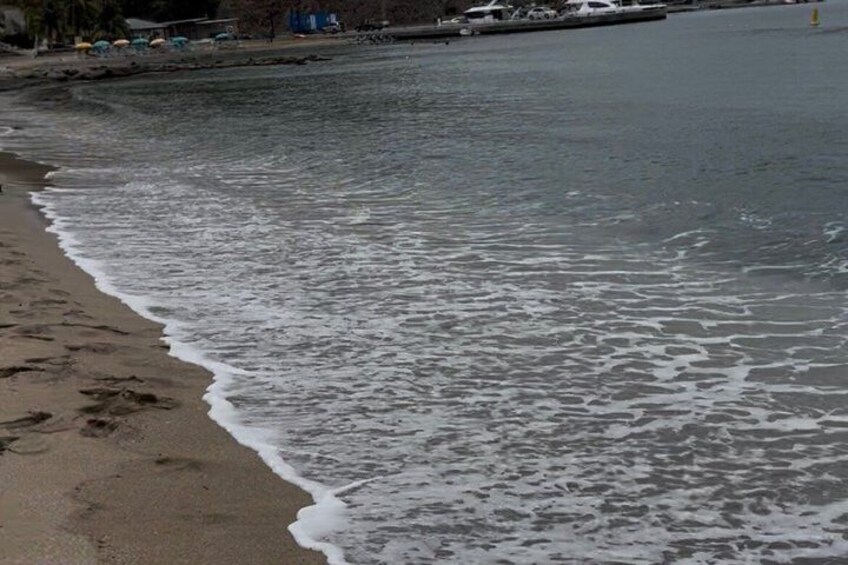 A beach with foamy waves, a sandy shore, and a distant shoreline with buildings and boats. 5