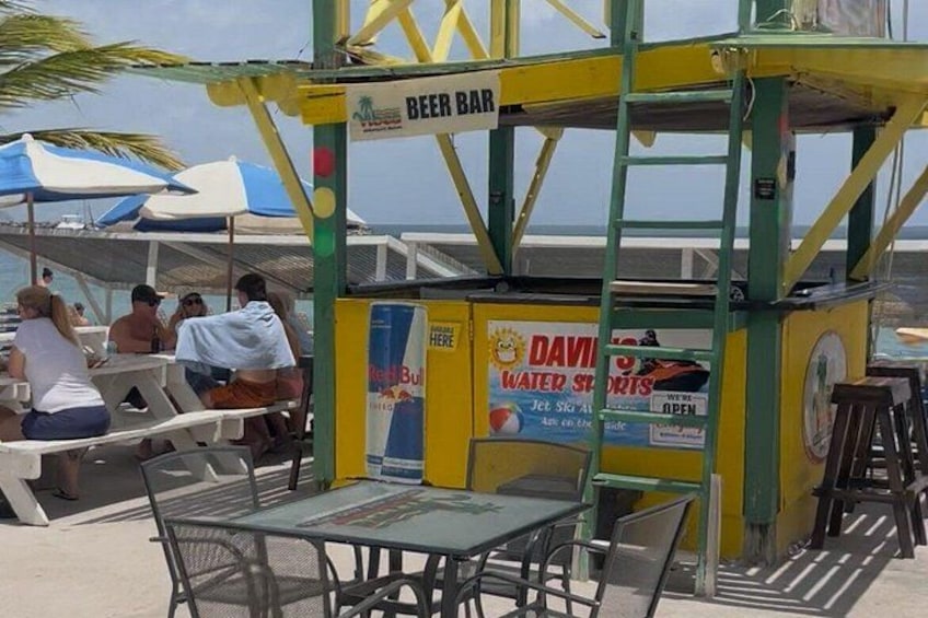 A beach bar with tables and chairs, a sign for a water sports rental, and a beer bar. 3