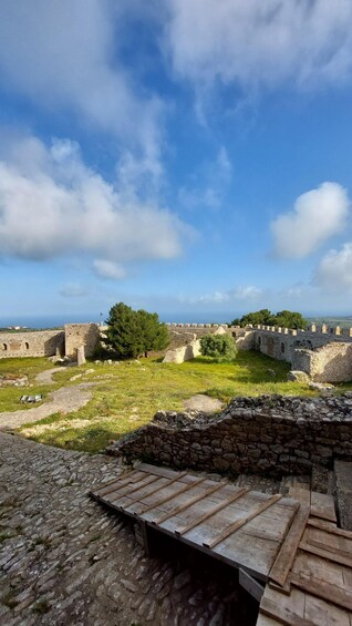 Ancient stone walls, a grassy field, and a clear blue sky with clouds. 5