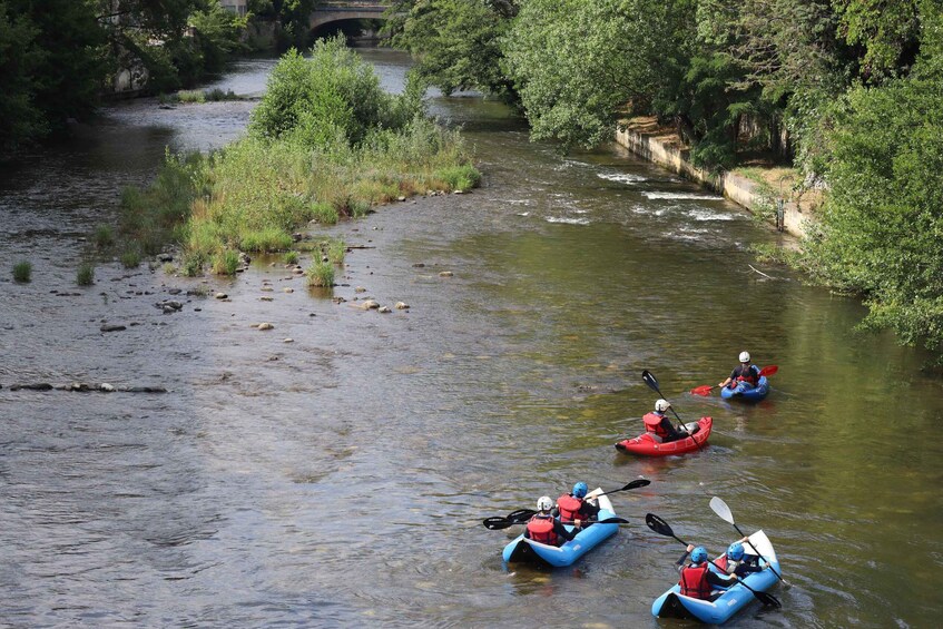 Three kayakers in blue and red kayaks on a calm river surrounded by greenery. 3