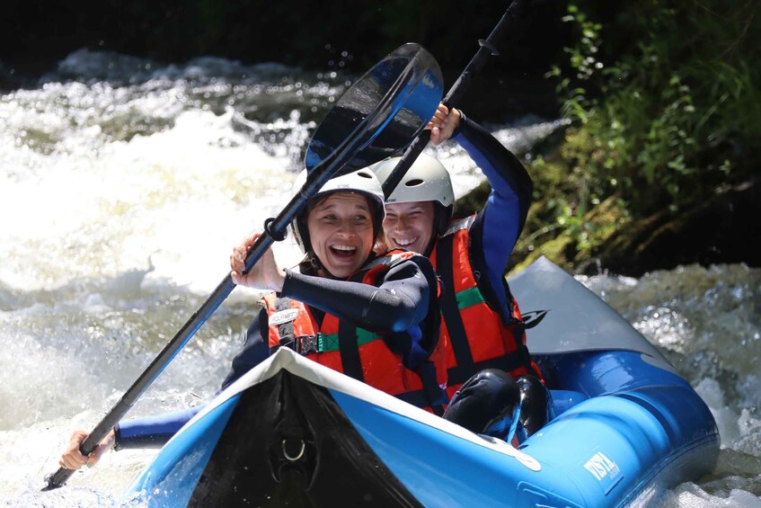 Two people in a blue inflatable raft navigating a whitewater river. 1