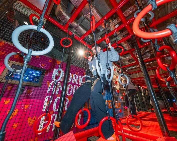 A person climbing a red and black obstacle course with rings and ropes. 3