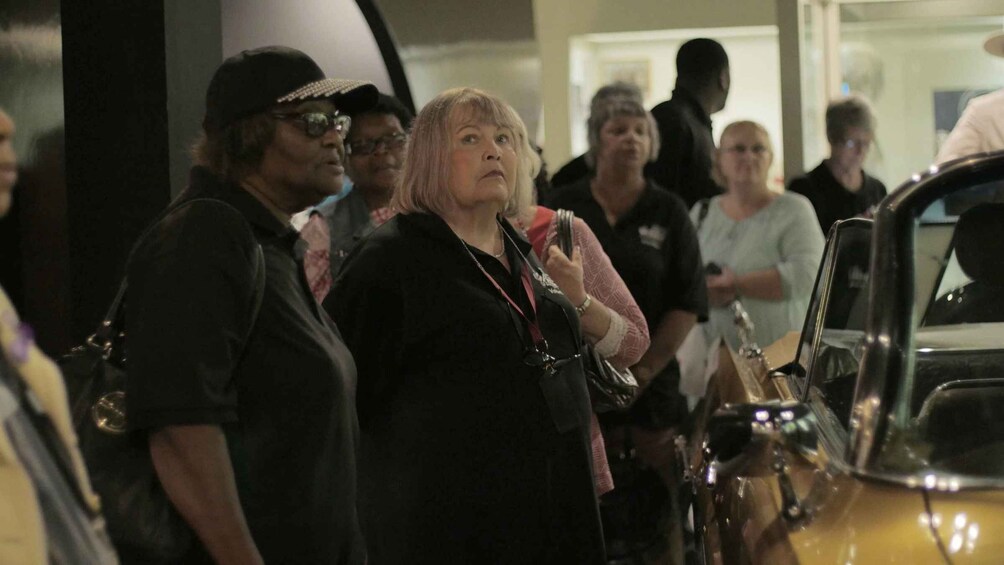 A group of people standing in an indoor setting, observing a vehicle. 5