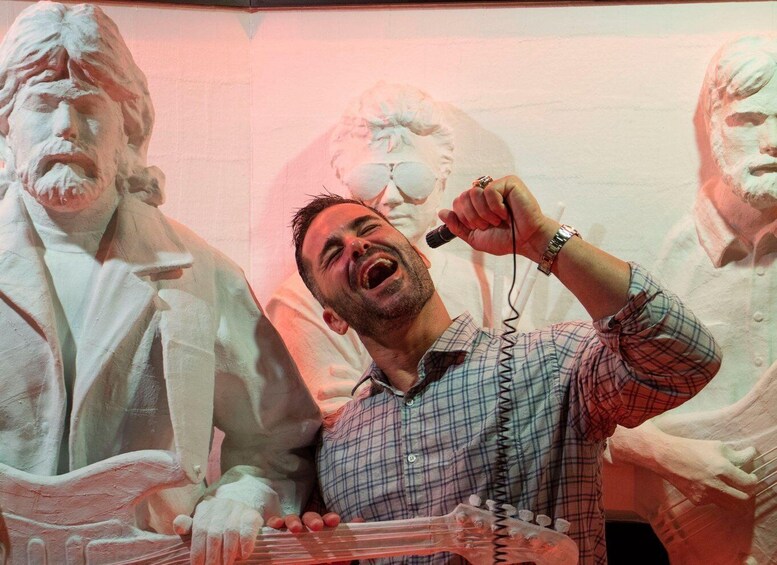 A person singing into a microphone with a guitar, surrounded by large white sculptures. 2