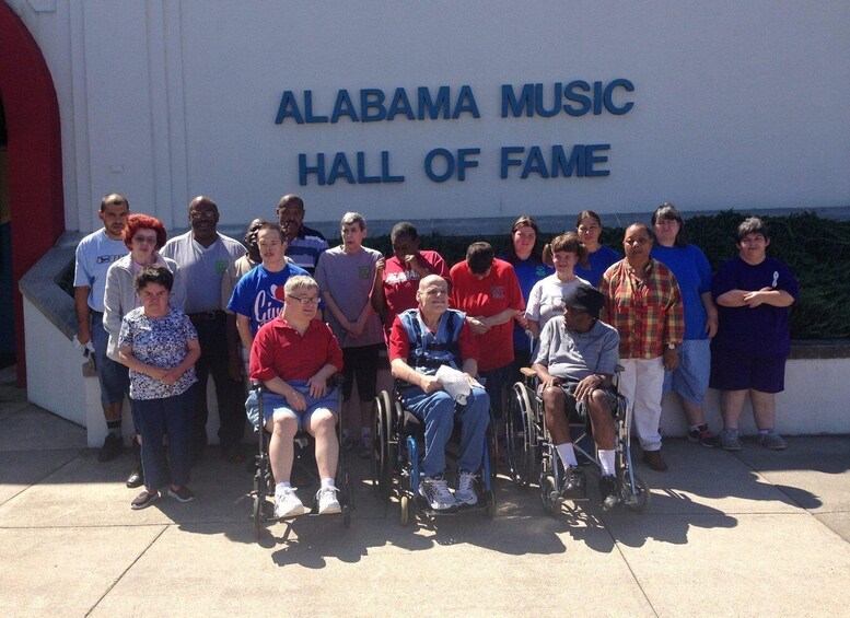 A group of people, some in wheelchairs, standing in front of the Alabama Music Hall of Fame. 4