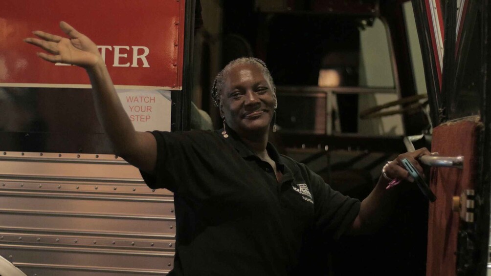 A person in a black shirt with a logo, standing next to a red truck with 'WATCH YOUR STEP' written on it. 3