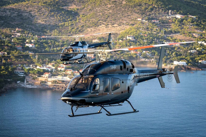 Two helicopters flying over a coastal area with houses and hills in the background. 2