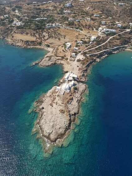 An aerial view of a coastal area with clear blue waters, rocky terrain, and scattered white buildings. 5