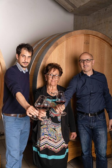 Three people holding wine glasses in a wooden barrel-shaped room. 4