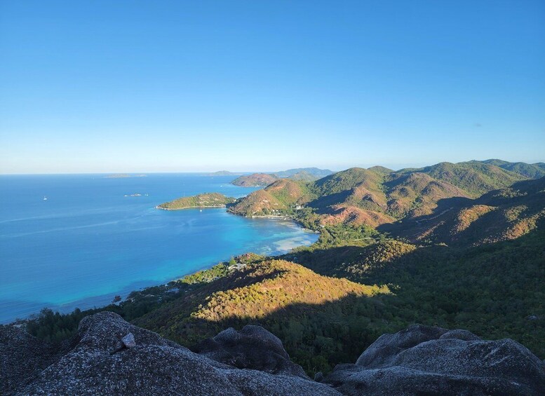 A coastal landscape with mountains, a clear blue sea, and rocky outcrops. 4