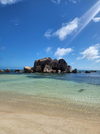 A clear blue sky, a sandy beach, and large rocks in the water. 2