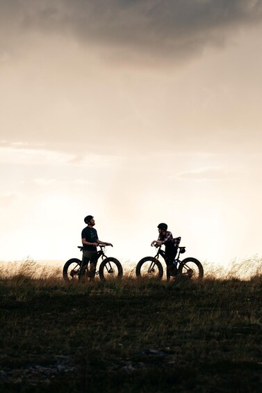 Two people on bicycles in a field with a cloudy sky. 2