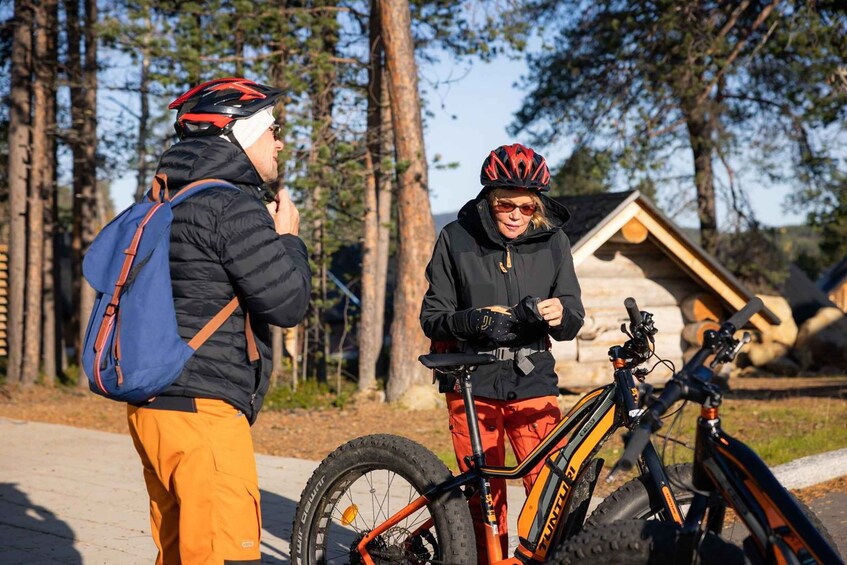 Two people standing by a wooden cabin with bicycles. 5