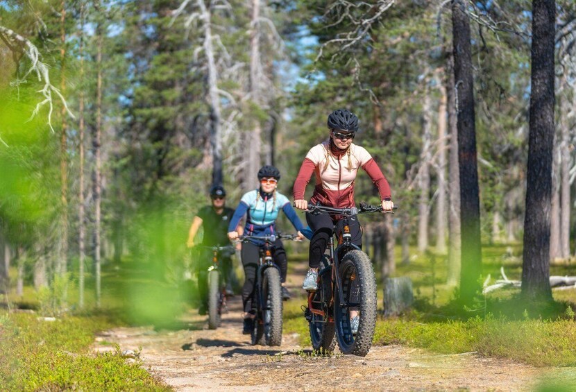 Three mountain bikers on a dirt trail surrounded by trees. 1