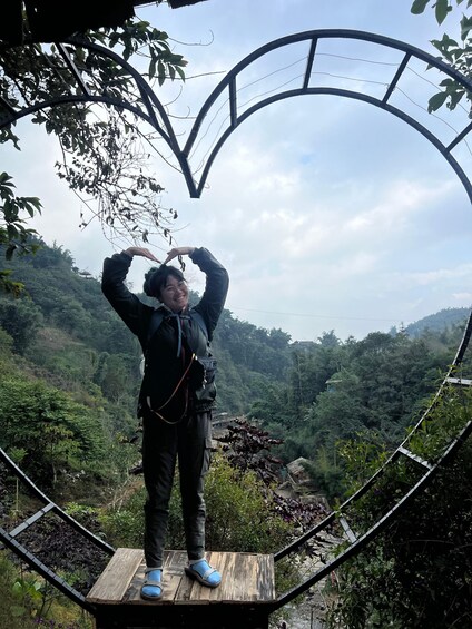 A person standing on a wooden platform with a heart-shaped metal structure behind them, overlooking a lush valley. 5