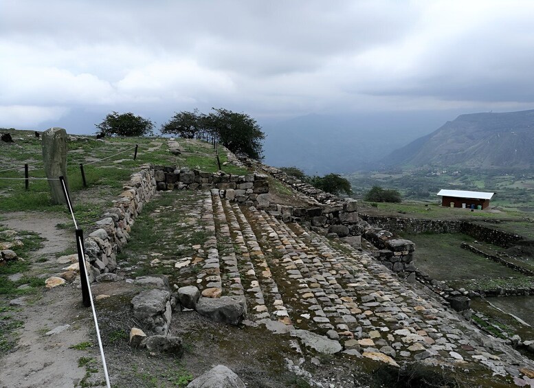 Ancient stone ruins with a stone wall and a small building in a mountainous landscape. 2