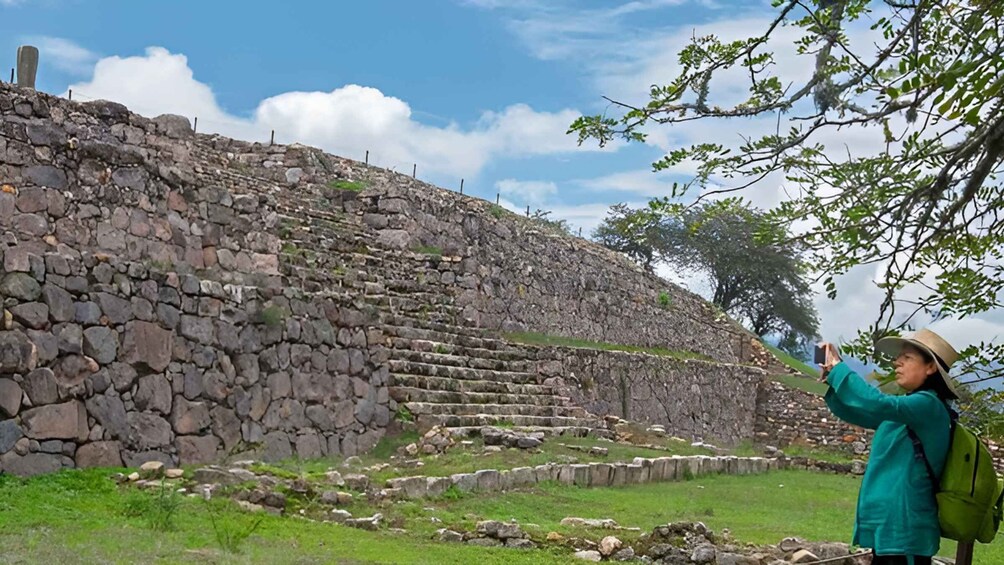 A stone structure with steps leading up to a flat area, surrounded by greenery and trees. 1