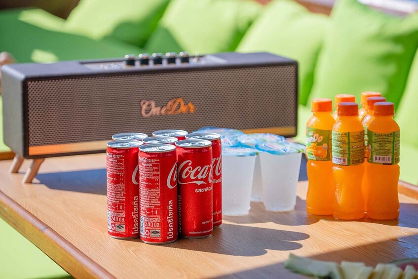 A wooden table with a speaker, cans of Coca-Cola, a pitcher of water, and bottles of orange juice. 5