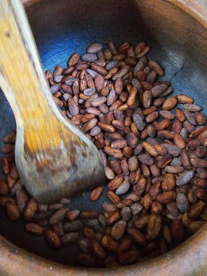 A wooden spoon stirring roasted coffee beans in a pan. 3