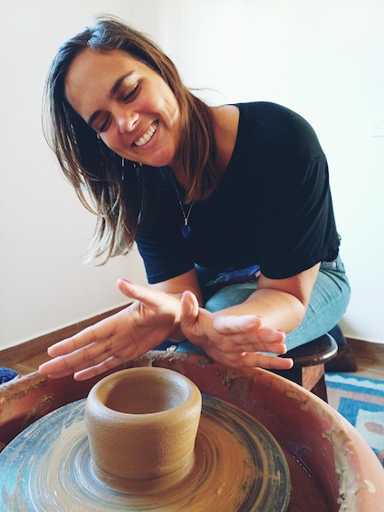 A person kneeling by a pottery wheel, shaping a clay pot. 2