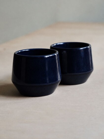 Two dark blue ceramic cups on a light wooden surface. 2