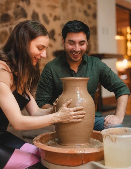 Two people working on a pottery wheel, shaping a clay pot. 1
