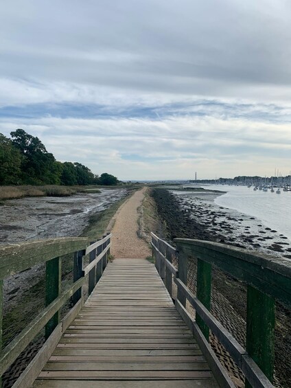 A wooden boardwalk leading to a beach with a rocky shoreline and boats in the distance. 1
