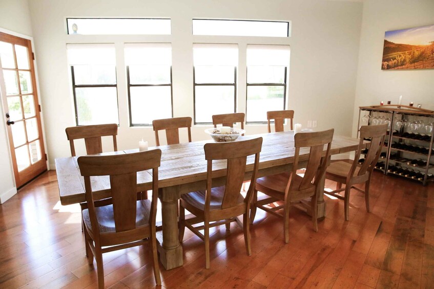 A dining room with a wooden table and chairs, large windows, and a wine rack. 2