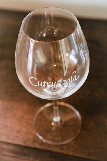 A clear wine glass with the inscription 'Cutruzzola VINEYARDS' on a wooden surface. 3